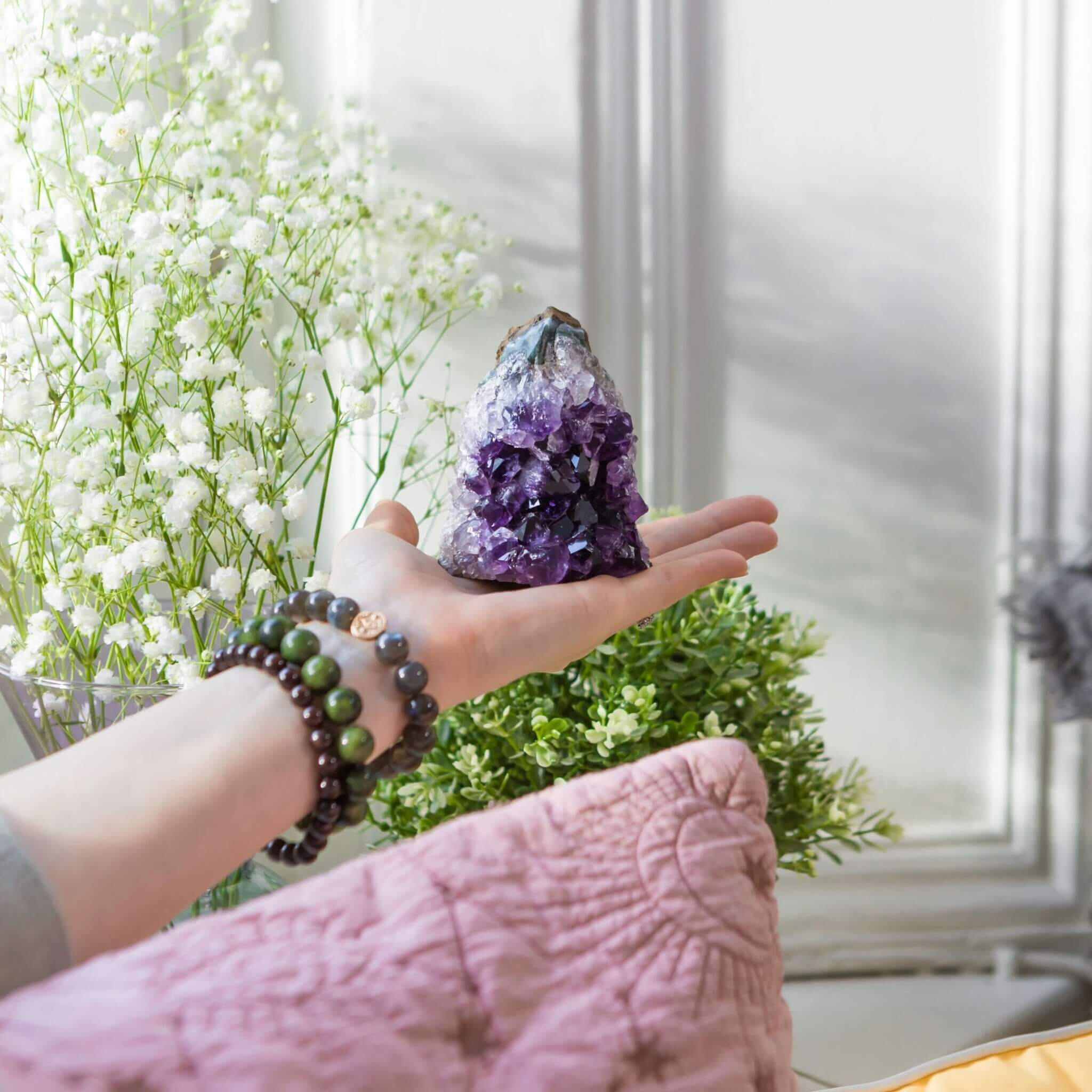 Healing Crystals Amethyst crystal cluster held by somebody wearing crystal bracelets.